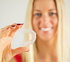 Woman in red shirt holding an Invisalign clear aligner