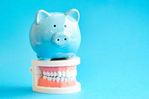 Piggy bank atop model teeth representing the cost of cosmetic dentistry in Falmouth