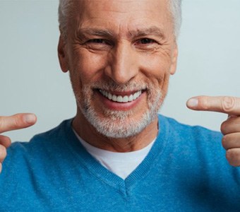 a man smiling and pointing at his new dentures