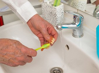 a person caring for his dentures by brushing them