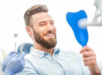 bearded man admiring his smile in the dental chair