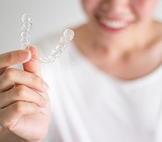 Woman in white shirt holding an Invisalign clear aligner