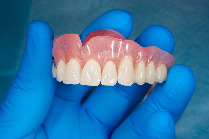 Gloved hands hold dentures for upper arch