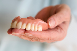 Close-up of a senior person’s hand holding dentures